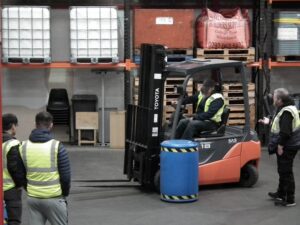 Photo of participants in a warehouse using a forklift Llun o gyfranogwyr mewn warws gan ddefnyddio fforch godi